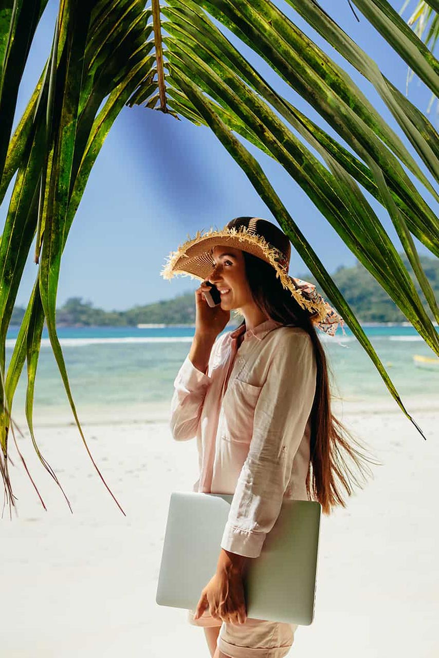 Woman gets in touch by phone while at the beach, palm trees and ocean view.